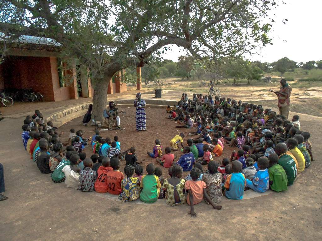 Ein Märchenabend im Operndorf Afrika. Kinder sitzen im Kreis. In dessen Mitte steht eine Sängerin